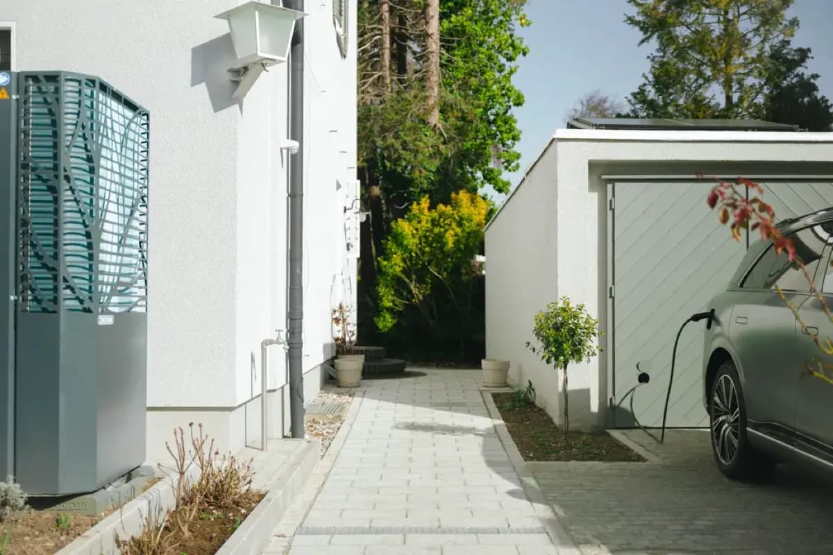 Wärmepumpe an der Hauswand, daneben Einfahrt mit Wallbox und Elektroauto
